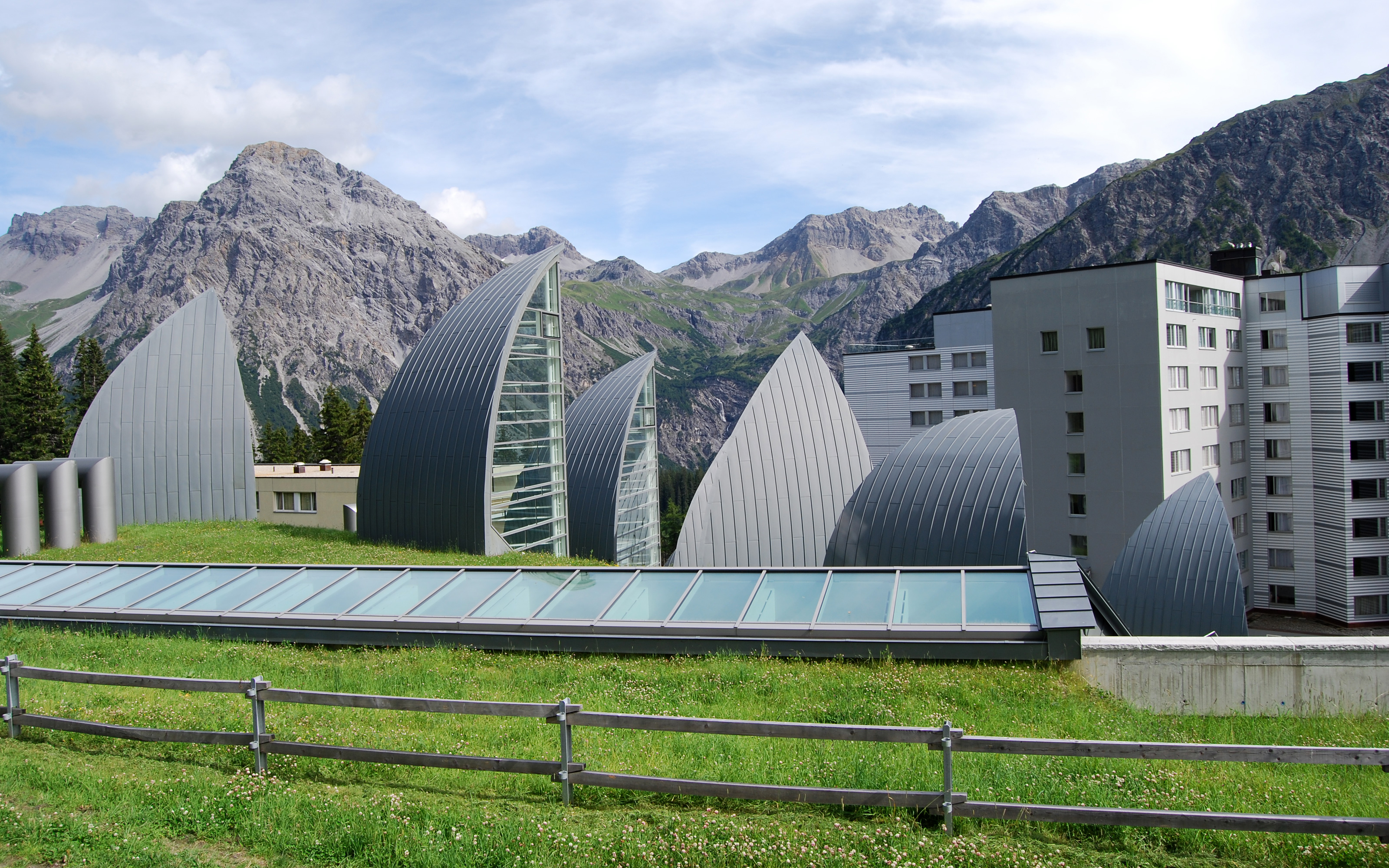 Sail-shaped skylights on a green roof in front of mountains
