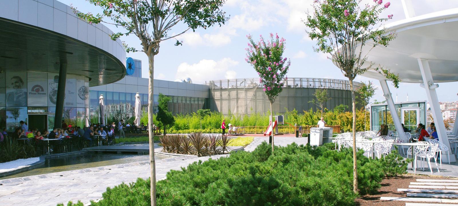 People sitting on a roof garden with walkways, blossoming small trees and shrubs